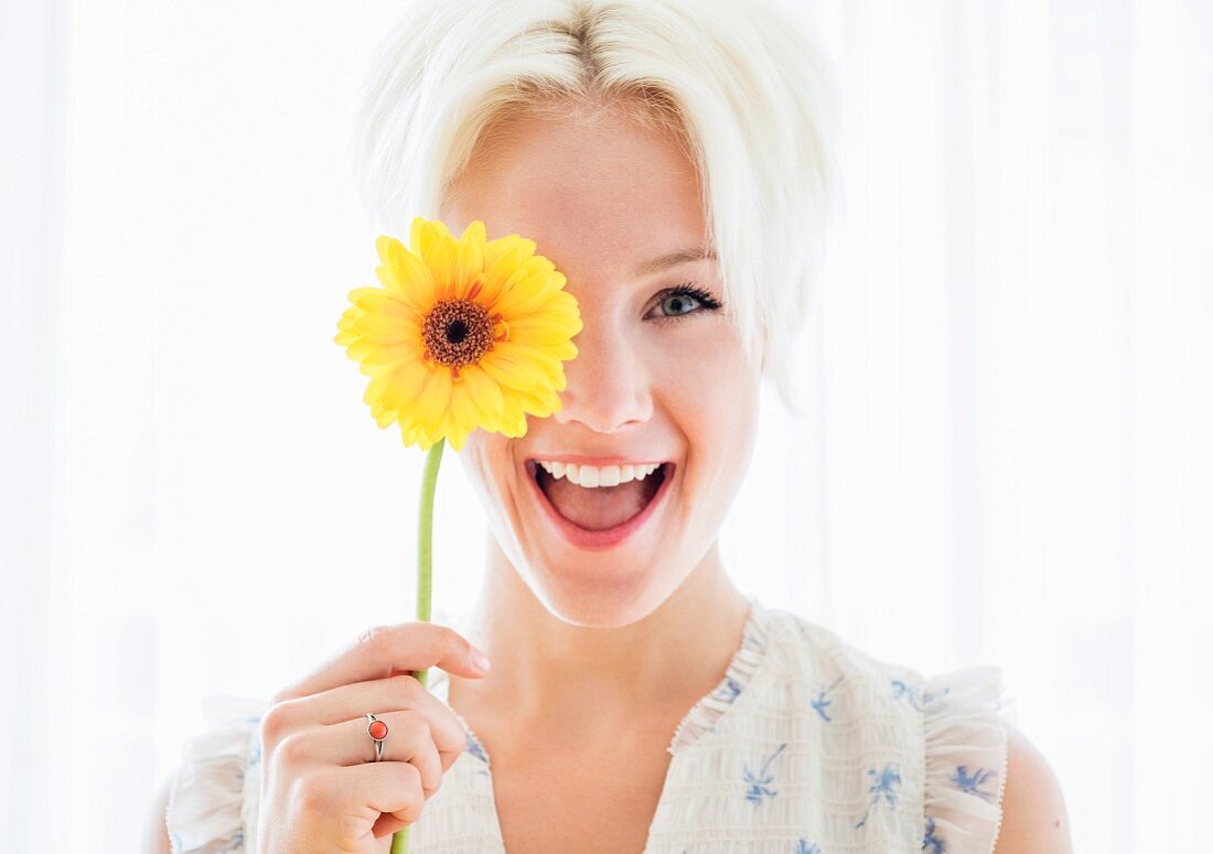 Junge, blonde Frau mit gelber Blume vor dem Auge