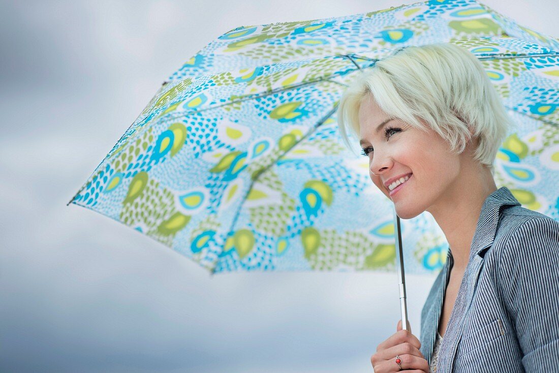 Junge, blonde Frau unter buntem Regenschirm