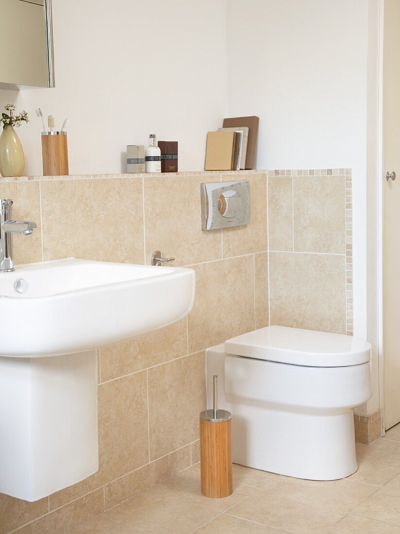 Sink and toilet on projecting wall with sand-coloured tiles in modern bathroom