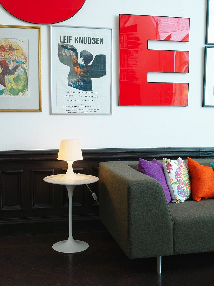 Tulip side table and dark grey couch with scatter cushions below decorative letters and artworks on wall above wainscoting