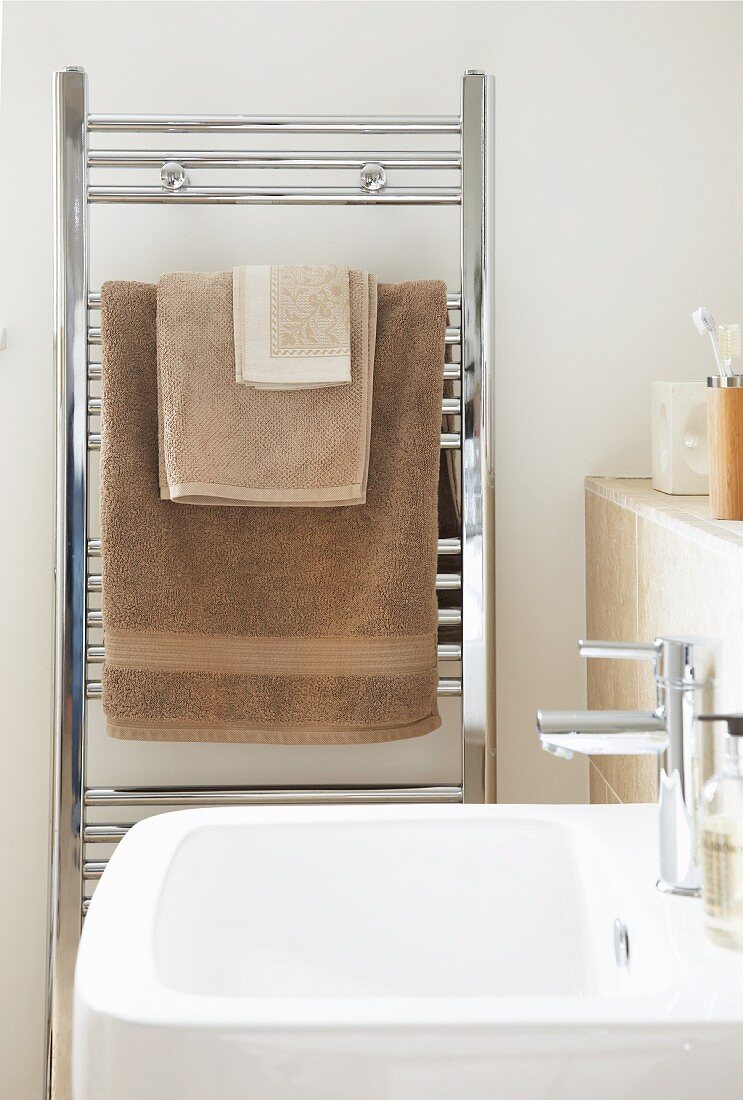 View across sink to stainless steel towel rack with towels of various sizes in shades of brown