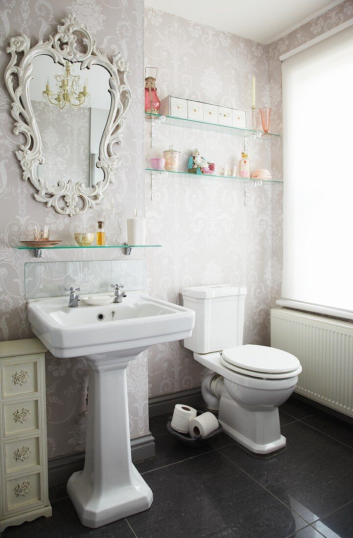 A light bathroom with an elaborate mirror and traditionally patterned wallpaper