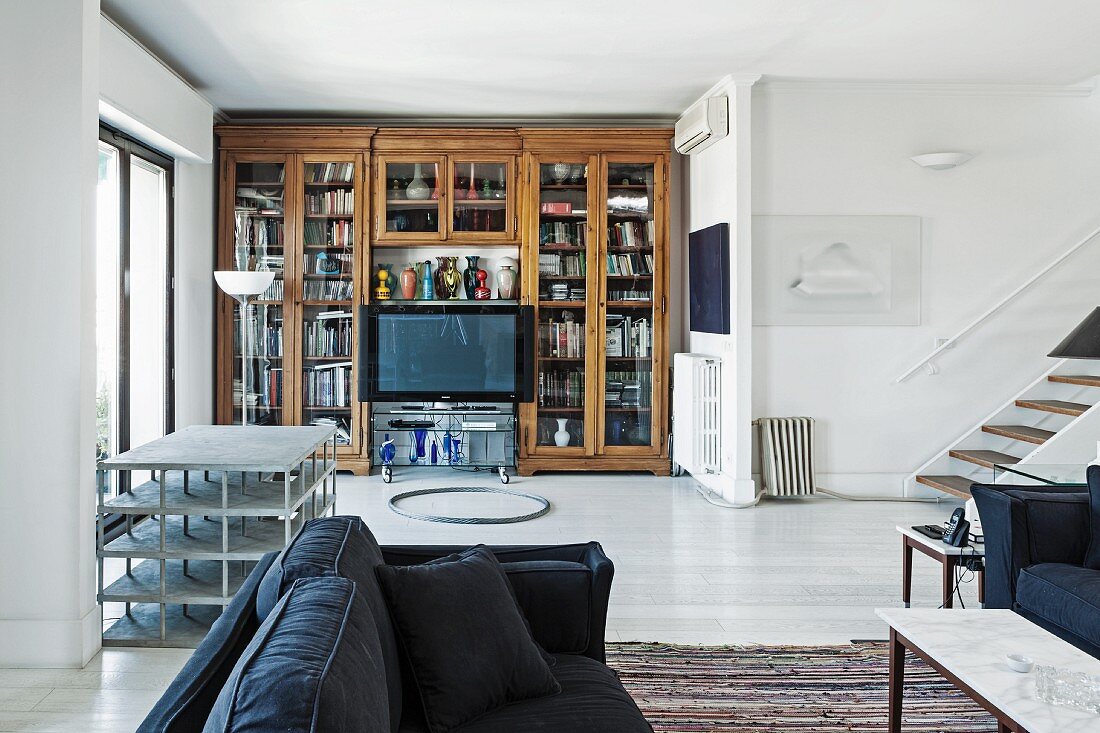 Dunkelblaues Sofa in offenem Wohnraum, im Hintergrund eingebauter Vitrinenbücherschrank und Flachbildschirm