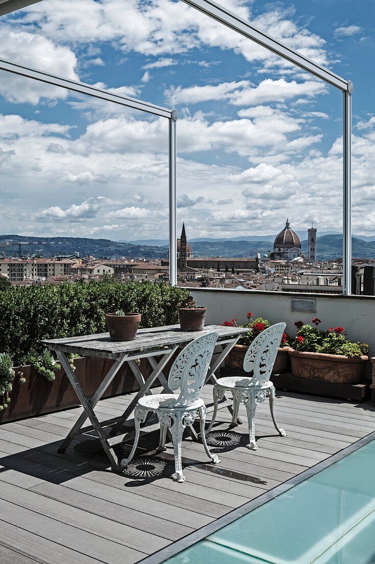 Sitzplatz mit Vintage Metallstühlen, weiss lackiert und verwitterter Holztisch auf Dachterrasse mit Blick auf Florenz