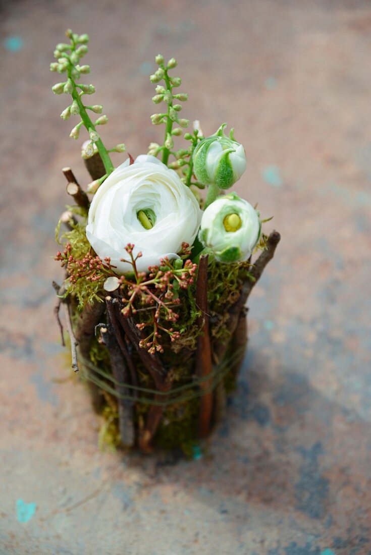 White ranunculus in jam jar covered in twigs and moss