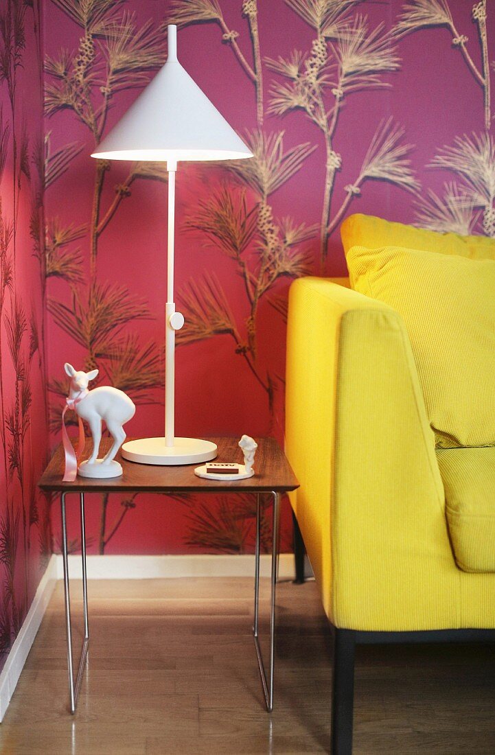 Yellow sofa and knick-knacks and lamp on side table against mauve wallpaper