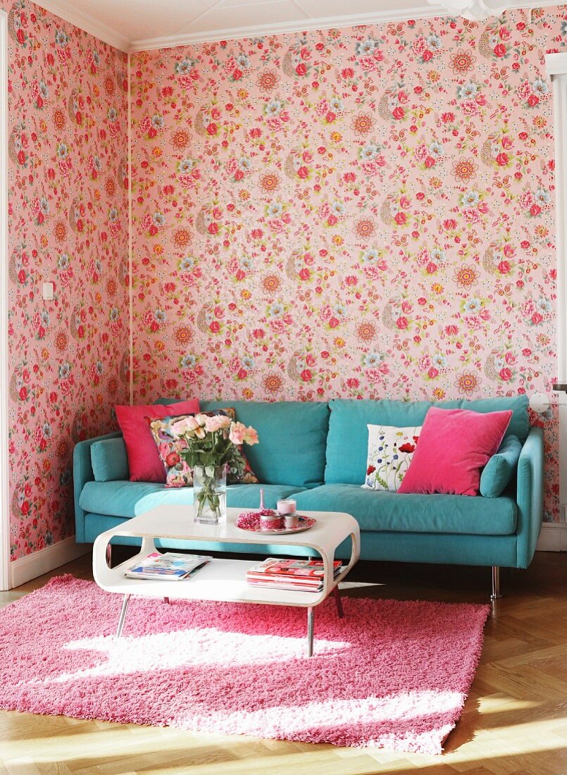 Weisser Retro Couchtisch vor türkisblauem Sofa in Wohnzimmerecke mit Blumentapete