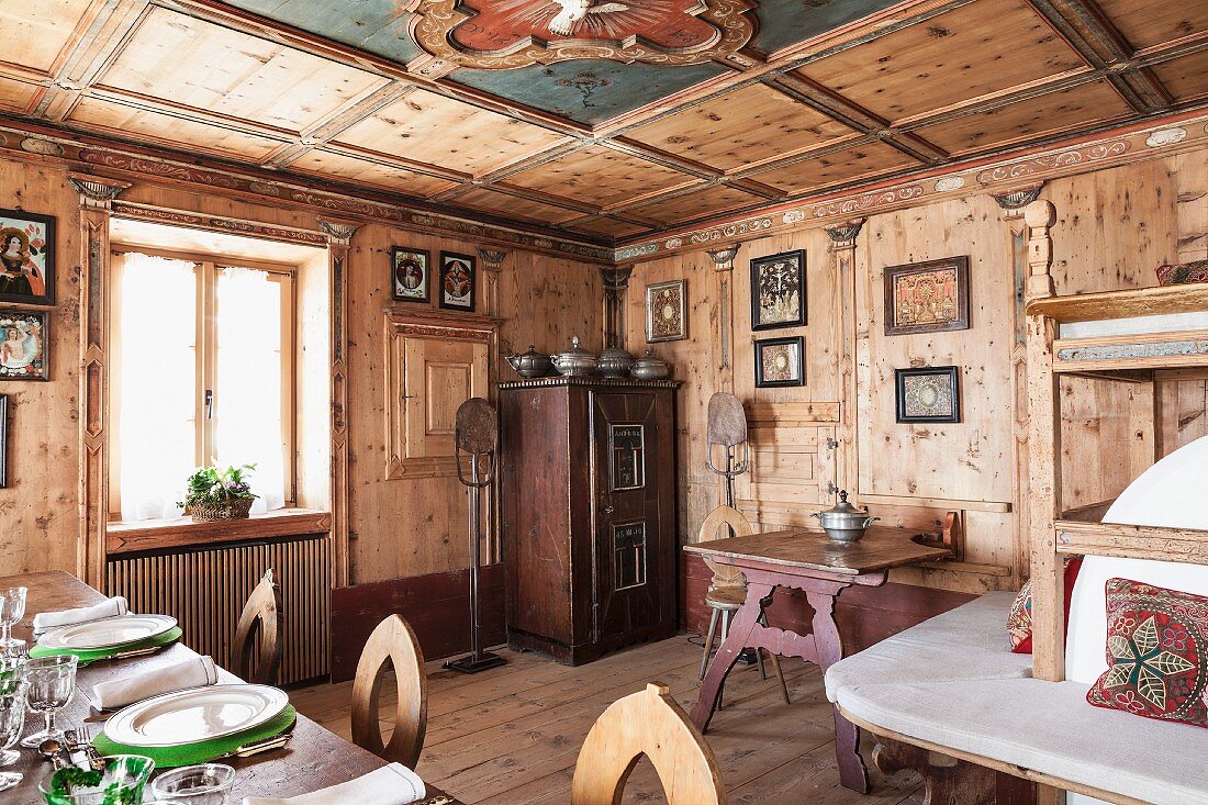 Holzvertäfelte Essstube mit antikem, bäuerlichem Mobiliar und Ofenbank; gedeckter Tisch im Vordergrund