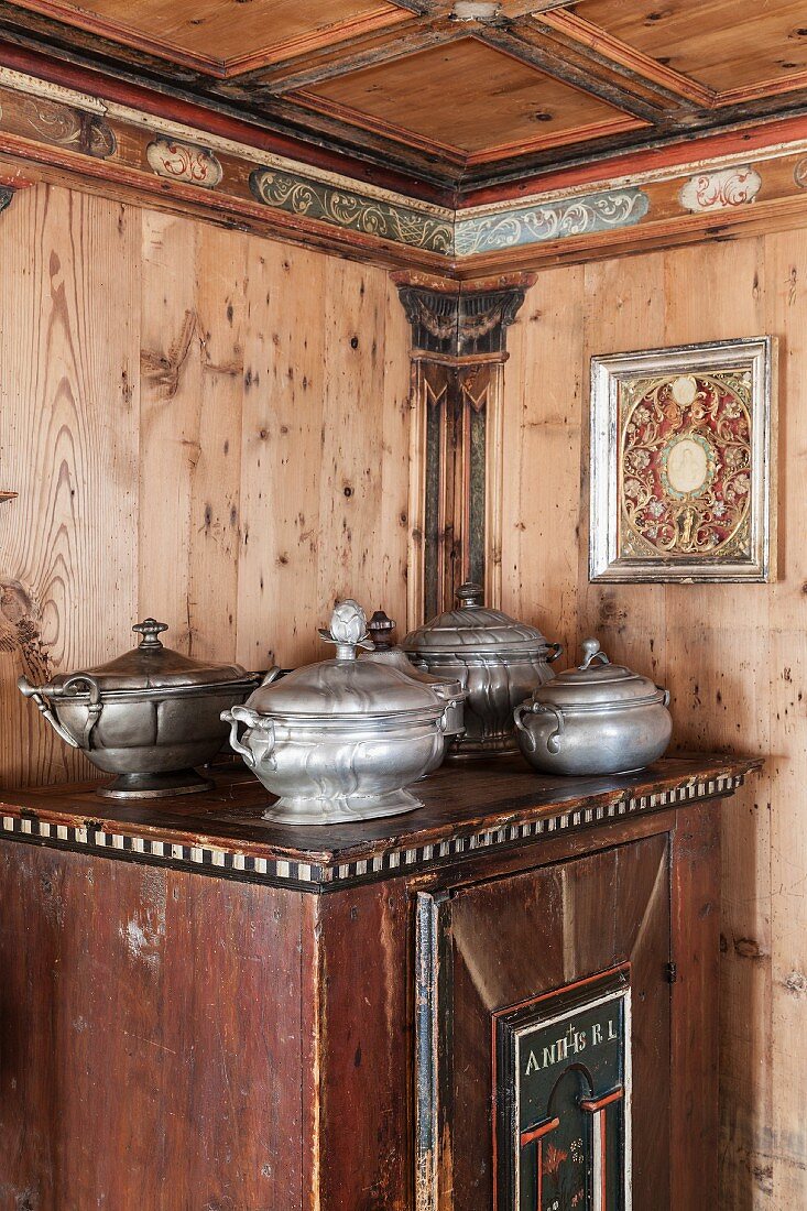 Pewter tureens on old farmhouse cupboard in wood-panelled dining room