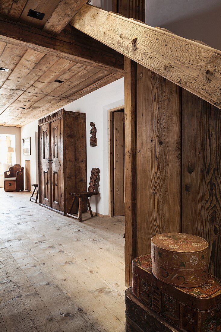 Hallway in restored farmhouse with antique furniture; stacked cases decorated with faded country-style painting in foreground