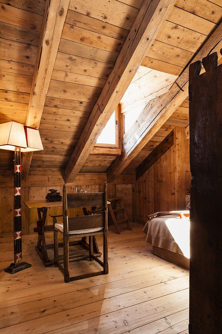 Artistically crafted standard lamp and simple workspace below wood-panelled sloping ceiling in chalet