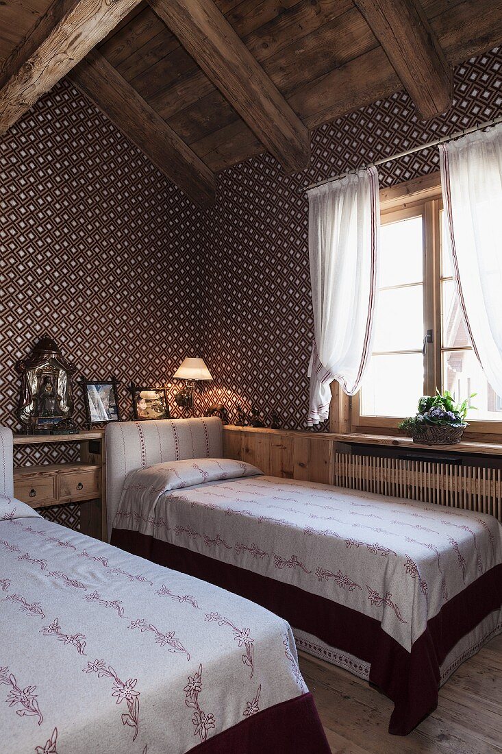 Textiltapete mit geometrischem Muster in Gästezimmer unterm Dach mit zwei Einzelbetten und romantischem Flair in restauriertem Chalet