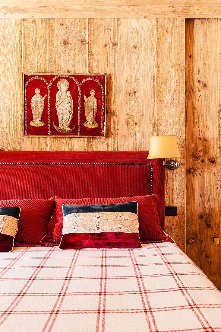 Religious triptych above red upholstered headboard of double bed; walls panelled in solid, plain wood