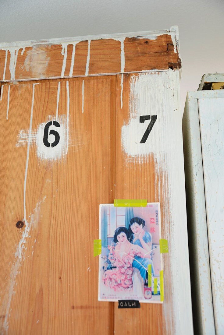 Rückansicht eines Holzschrankes mit Zahlen, darunter Postkarte mit gelben Klebestreifen