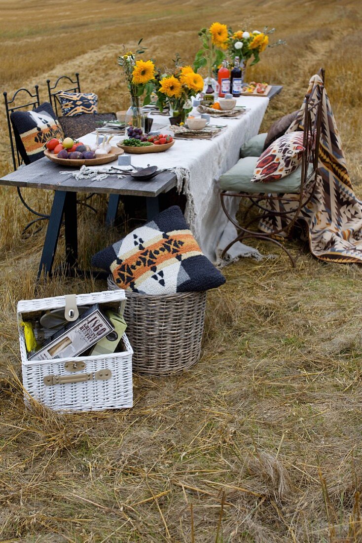 Gedeckter Tisch mit Sonnenblumen und weisser Leinentischdecke auf Stoppelfeld