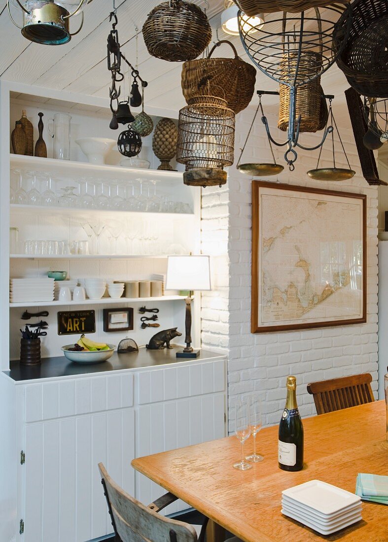 Holztisch unter Korbsammlung an Decke aufgehängt und eingebautes Küchenbuffet in Nische neben geweisselter Ziegelwand