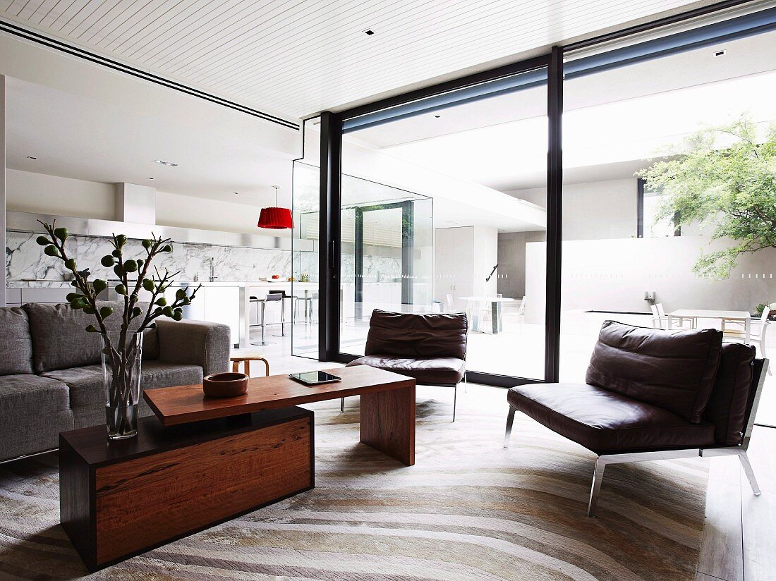 Sitzbereich mit Ledersesseln und variablem Coffeetable vor Schiebetürfront eines offenen Wohnraumes mit Blick in Innenhof