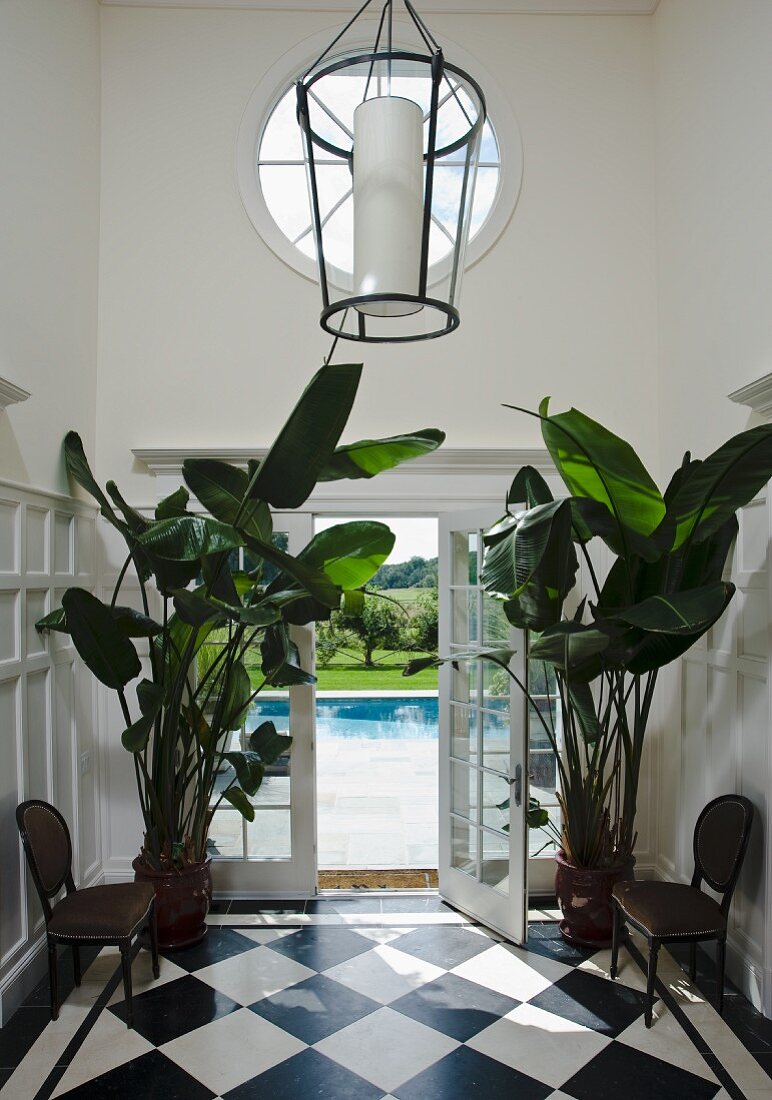 Diele mit schwarzweissem Schachbrettboden und Pflanztöpfen mit Bananenpflanzen; Blick auf Pool durch geöffnete Fenstertür