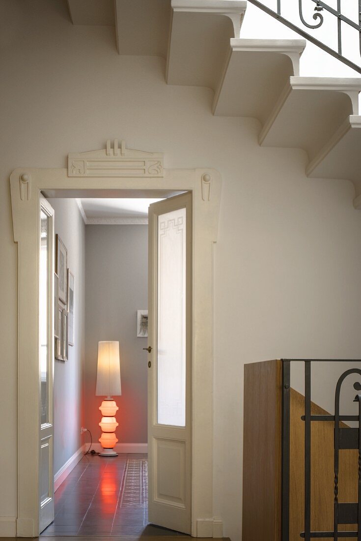 Weisser Türrahmen in Art Deco; in der Zimmerecke eine moderne Stehlampe mit roten Lichtkörpern