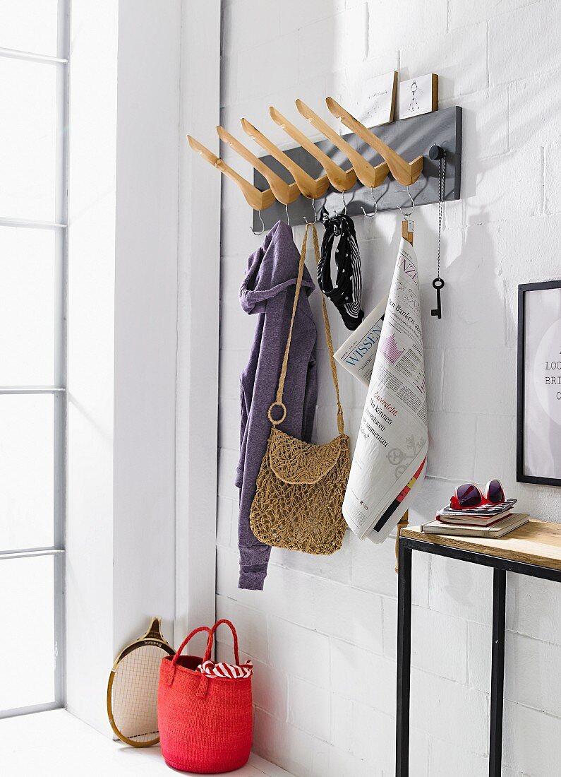 Selbstgebaute Garderobe aus Holz-Kleiderbügeln auf schwarzem Brett, daneben schmaler Wandtisch an geweisselter Ziegelwand
