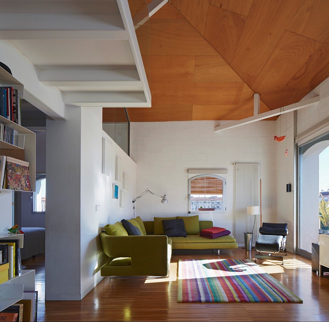 Moosgrüne Sofalandschaft und buntgestreifter Teppich in zweigeschossigem Wohnraum mit Galeriegeschoss