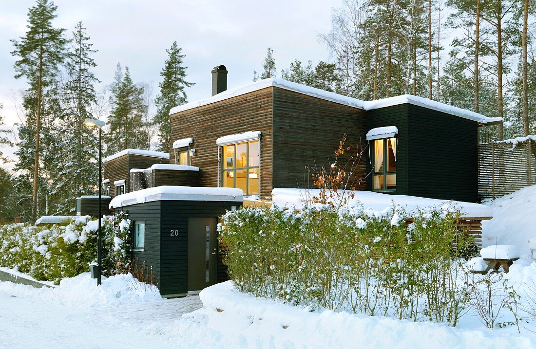 Mit dunklem Holz verschaltes, modernes, skandinavisches Flachdachhaus in verschneiter Winterlandschaft