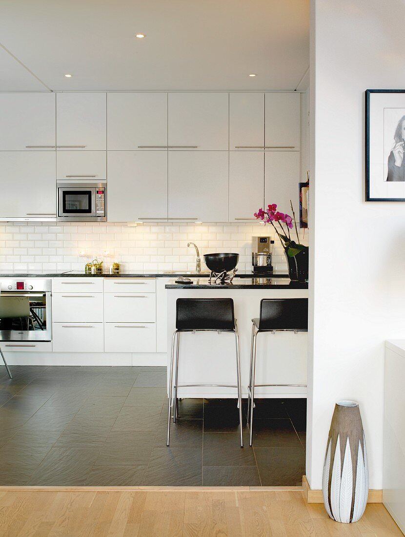 weiße, moderne Einbauküche mit Fliesenboden, Arbeitsplatte und Barhockern in Kontrastschwarz