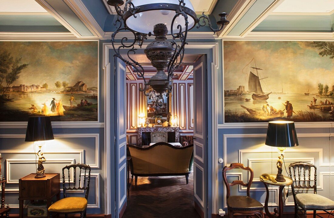 Esszimmer mit historischen Gemälden in blauweisser Holzvertäfelung und antiker Gaslampe; Blick in den angrenzenden Salon
