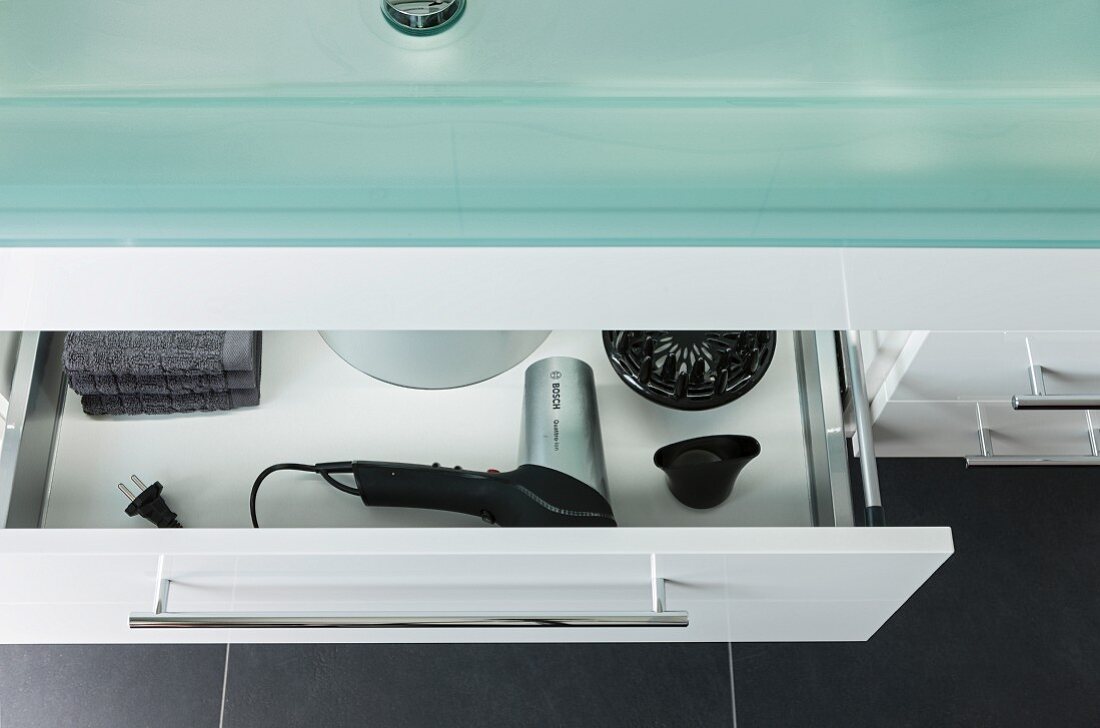 Detail of washstand with a glass top and a half open drawer with a view of a hairdryer and accessories