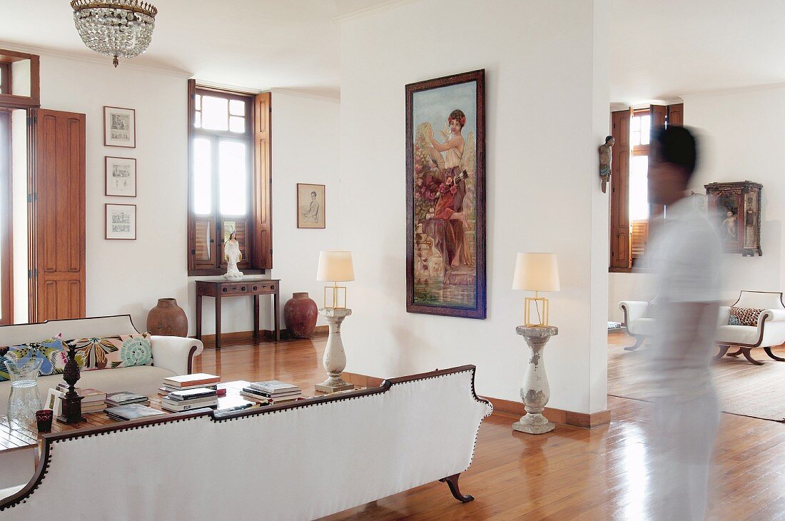 White sofa set in elegant foyer with portrait format artwork on partition between table lamps on stone plinths