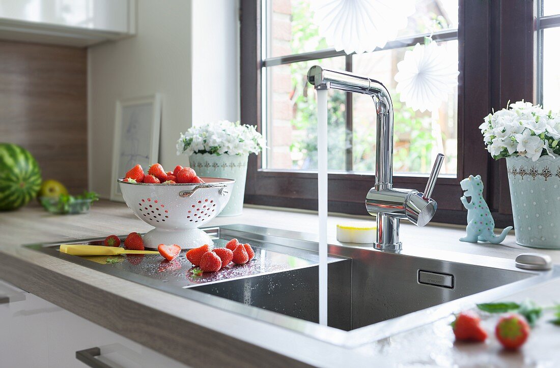 A square sink with the tap running and freshly washed strawberries in a white colander