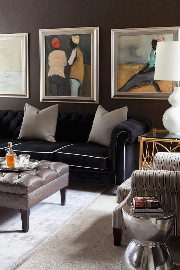 Gepolsterter Couchtisch vor elegantem, schwarzem Sofa mit grauen Kissen, gerahmte Bilder an schwarz getönter Wand