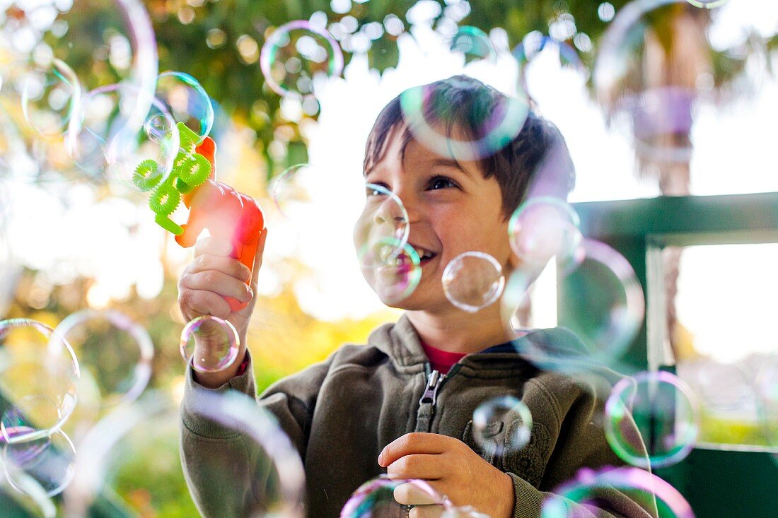 Kleiner Junge spielt mit Seifenblasen im Garten