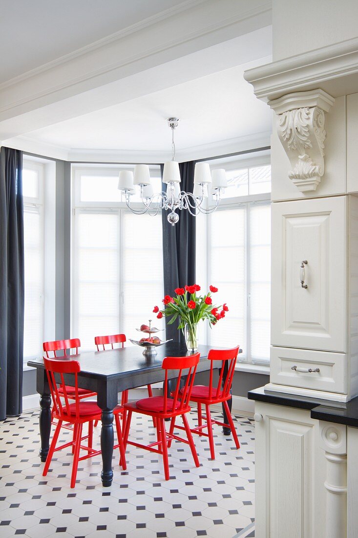 Schwarzer Holztisch und rote Holzstühle auf schwarz-weißem Fliesenboden im eleganten Erkerberiech