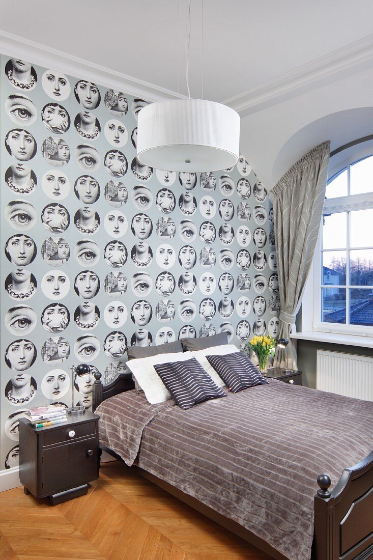 Double bed with grey, velvet throw against wallpaper with pattern of women's faces