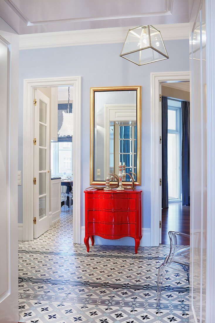 Vorzimmer mit gemustertem Fliesenboden, an Wand rote Kommode in postmodernem Stil, zwischen offenen Zimmertüren
