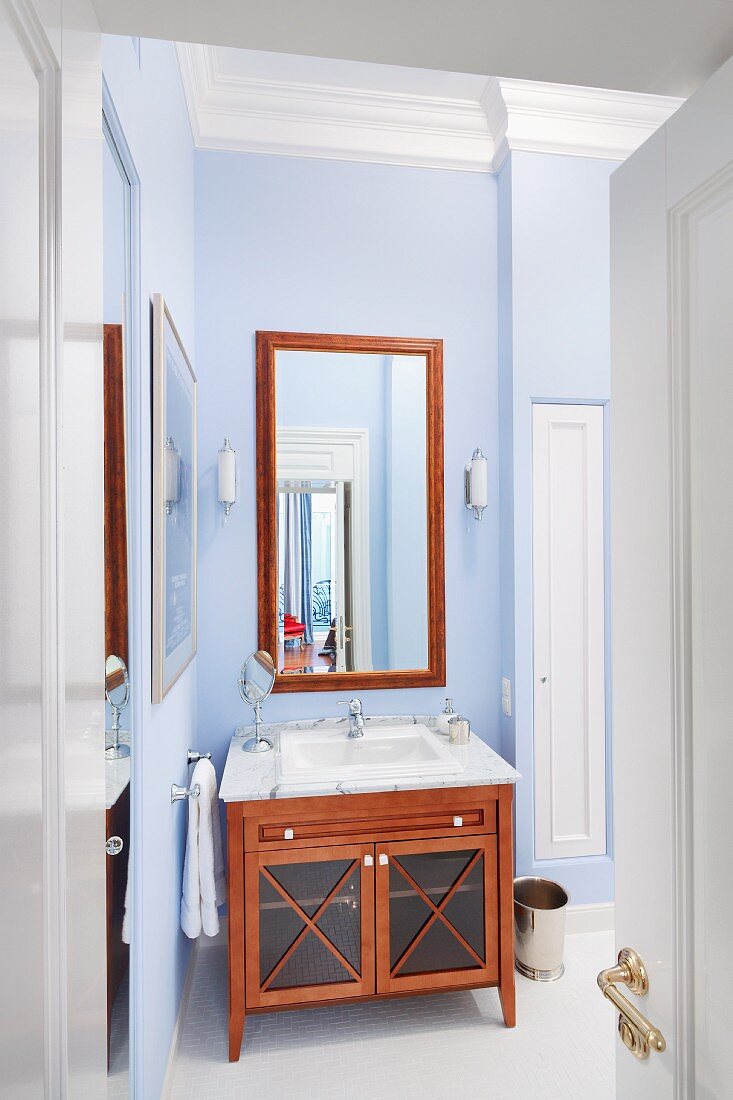 Blick durch offene Tür ins Bad, auf Waschtisch mit Unterschrank aus mahagonyfarbenem Holz vor hellblau getönter Wand