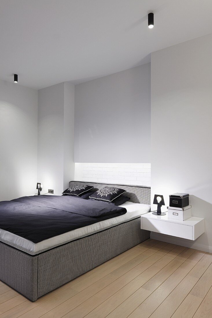 Minimalistisches Schlafzimmer mit Boxspringbett, schwarz-weiße Bettwäsche, seitlich an Wand schwebende Nachttischablage