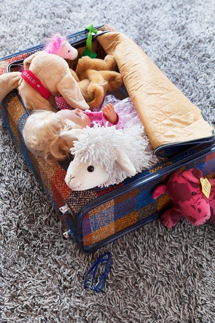 Offener Koffer mit Kuscheltieren und Puppe auf Teppich