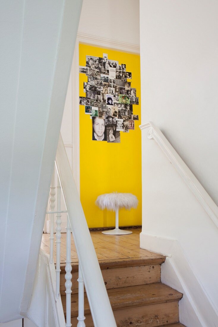 Treppenlauf in altem skandinavischen Wohnhaus mit Blick auf Fotocollage an gelb getönter Wand