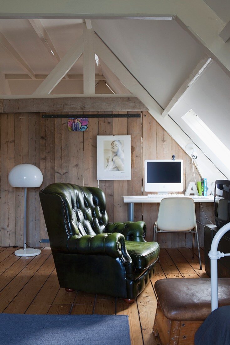 Green leather lounge chair in teenager's attic room; computer on desk against wooden board wall in background