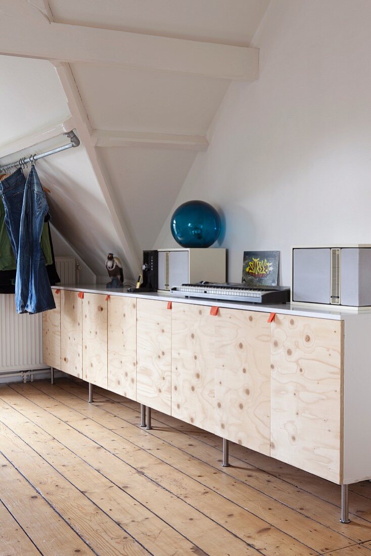Keyboard und Boxen auf Sideboard in Dachraum - Fronten in Naturholz mit Stofflaschen als Griffe; Jeans an Metallstange aufgehängt