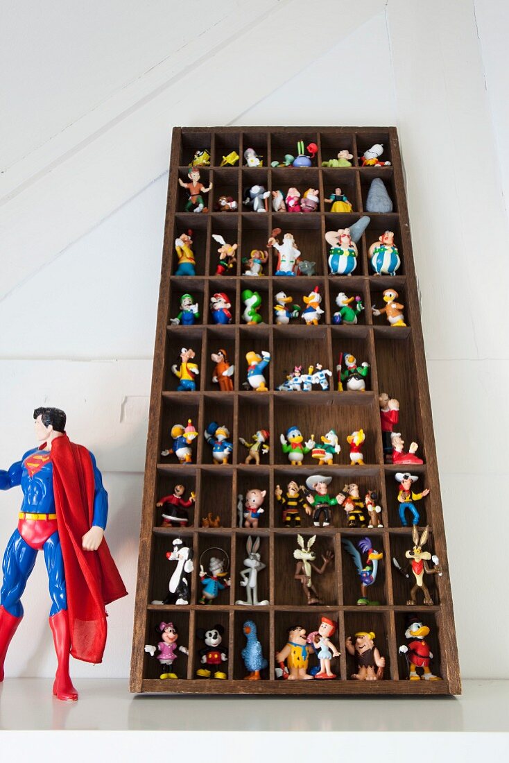 Sammlung bunter Comic-Figuren in einem Setzkasten, daneben stehend eine Superman-Figur