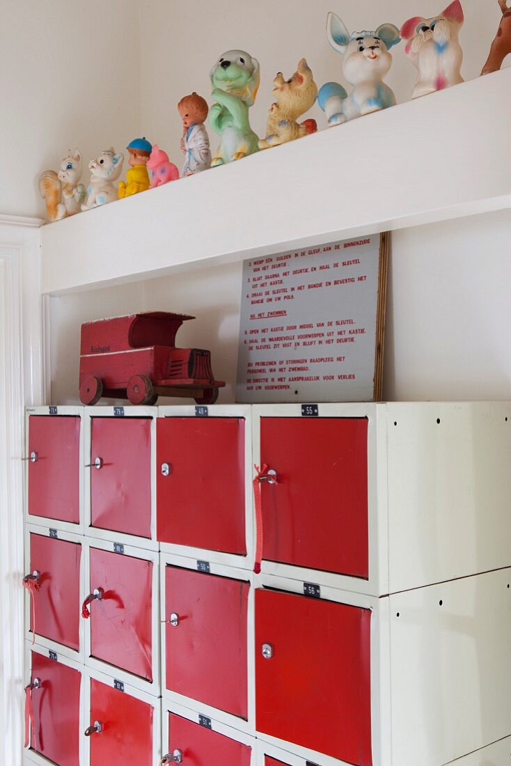Spielzeugauto auf ausrangiertem Schließfachschrank mit rot lackierten Türen; darüber auf einem Balken eine Sammlung Quietschfiguren