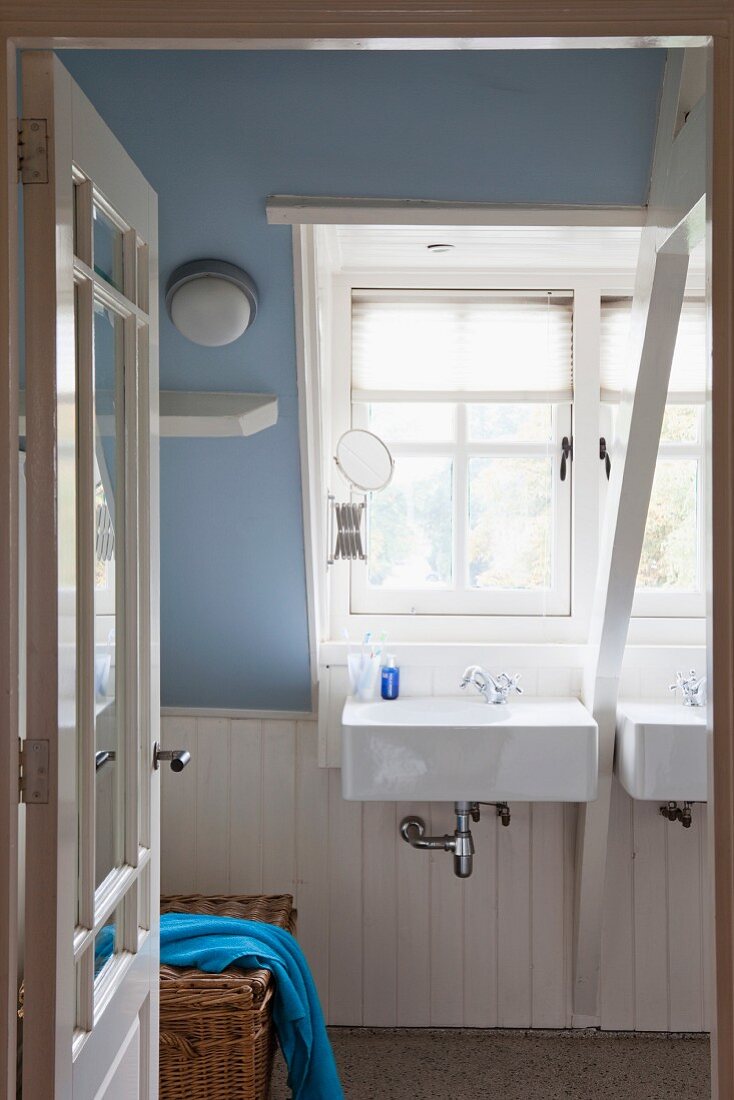 Sinks below dormer window in bathroom with white-painted wood and sloping ceiling painted lavender blue
