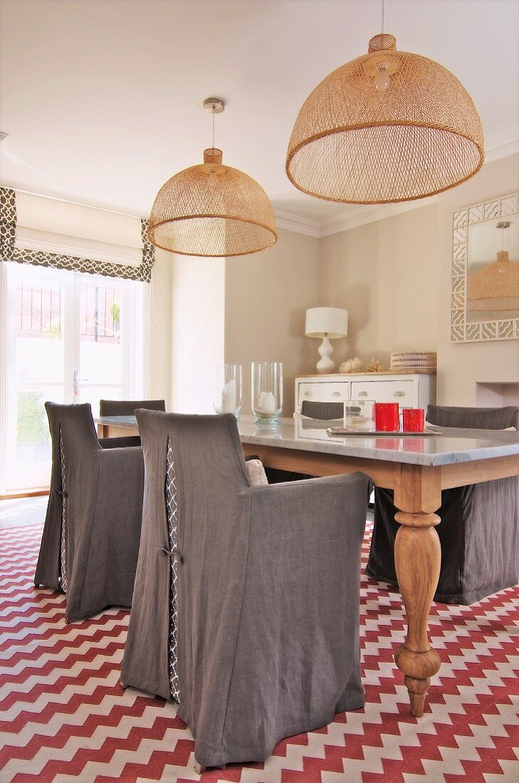 Graue Hussenstühle um Esstisch mit zwei Korbpendelleuchten, Teppich mit rotweissem Zickzackmuster im Landhausambiente