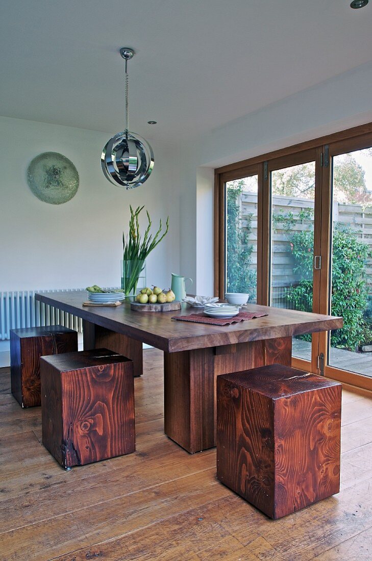 Custom dining table and cubic, red wood stools next to terrace doors