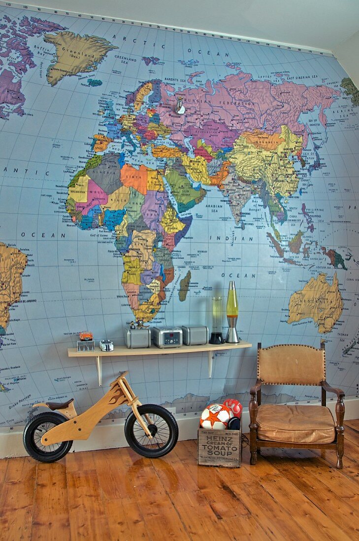Antiker Sessel neben Spielkiste und Laufrad, Wandkonsole an Wand mit Weltkarte Tapete