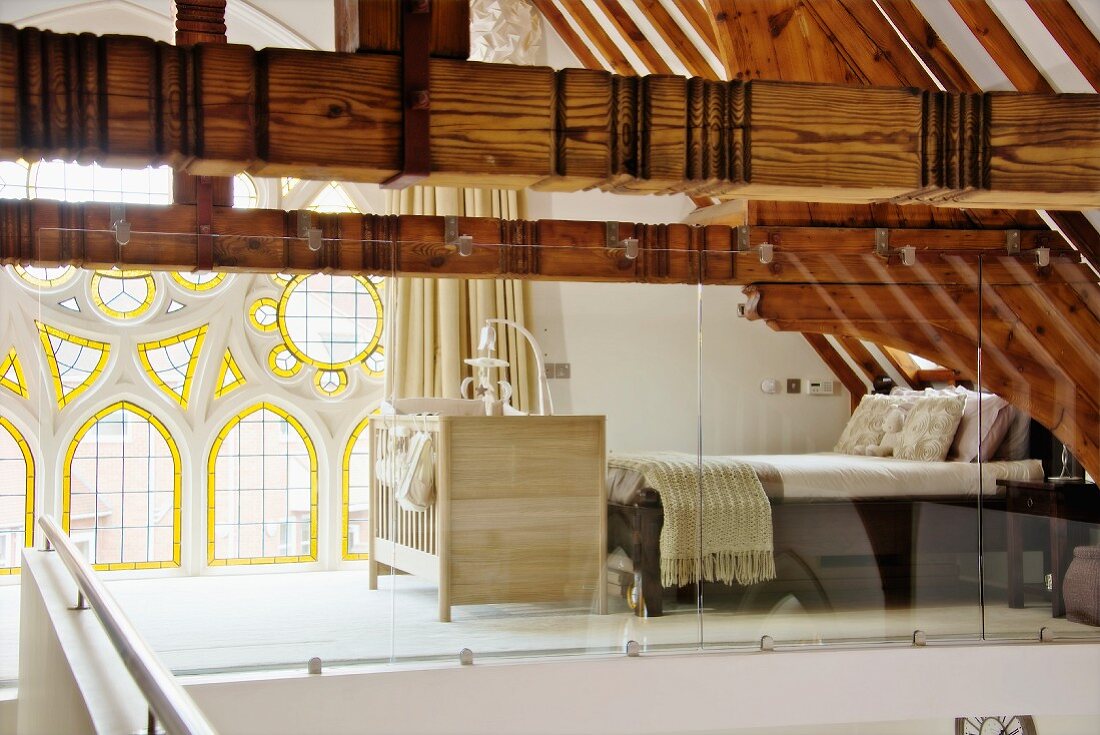 Blick in Schlafbereich auf Galerie, hinter Glastrennwand, alte Holzkonstruktion und neogotisches Fenster mit Rosetten und Buntglaselementen