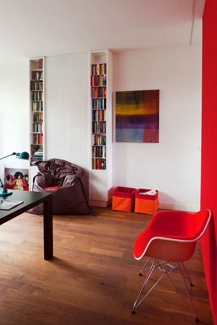 Roter Armlehnstuhl im Klassikerstil an roter Wand, im Hintergrund schmale Bücherregale in Weiß, und Aufbewahrungskisten vor Wand, in modernem Ambiente